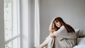 Mujer sentada junto a una ventana, envuelta en una manta clara y con expresión serena, simbolizando la reflexión sobre cuándo lo normal deja de sentirse normal