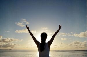 Mujer de espaldas con los brazos levantados hacia el cielo al amanecer, simbolizando libertad, esperanza y el aprendizaje de vivir sin miedo