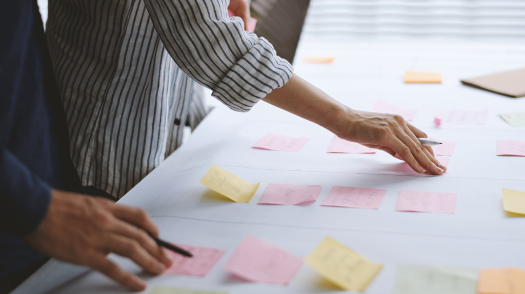 Manos de un equipo de trabajo planificando una estrategia de marketing con post-its. Representación de la metodología de planificación para pymes.